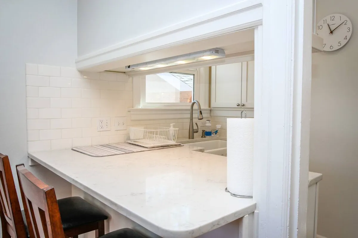 A bright, welcoming kitchen with a marble countertop, kitchen sink beneath a window, and bar stools lined up at the counter. The space is open and inviting, suggesting a place for casual dining or socializing before heading out to explore.