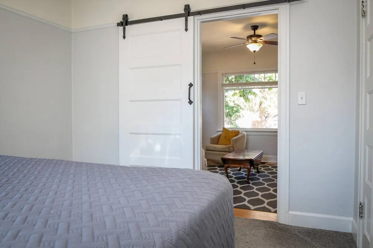 A bright, stylish interior with a king-size bed, a cozy armchair beside a window, and a rustic sliding barn door. The setup invites relaxation and highlights the comfort awaiting travelers after a day spent downtown.