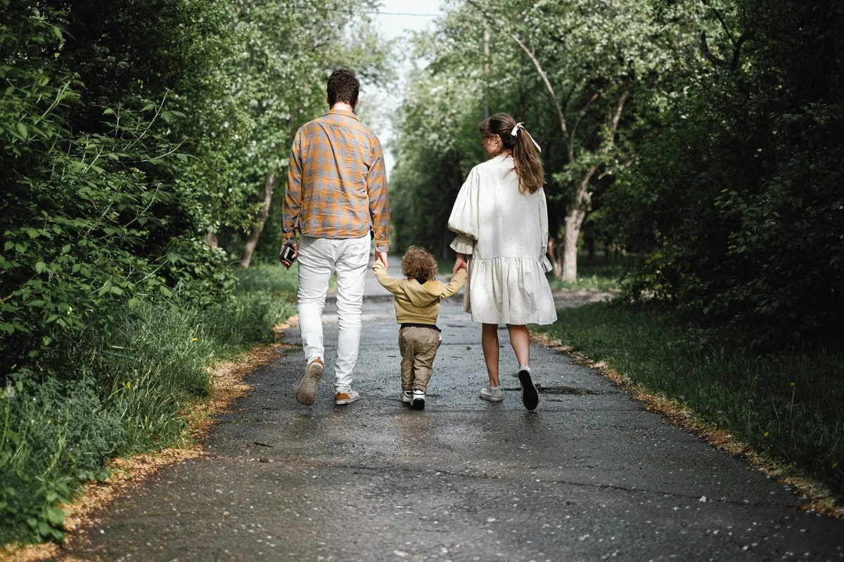 A family is seen walking together along a lush, green paved path surrounded by trees, suggesting a peaceful, friendly neighborhood with ample space to unwind and enjoy the outdoors.