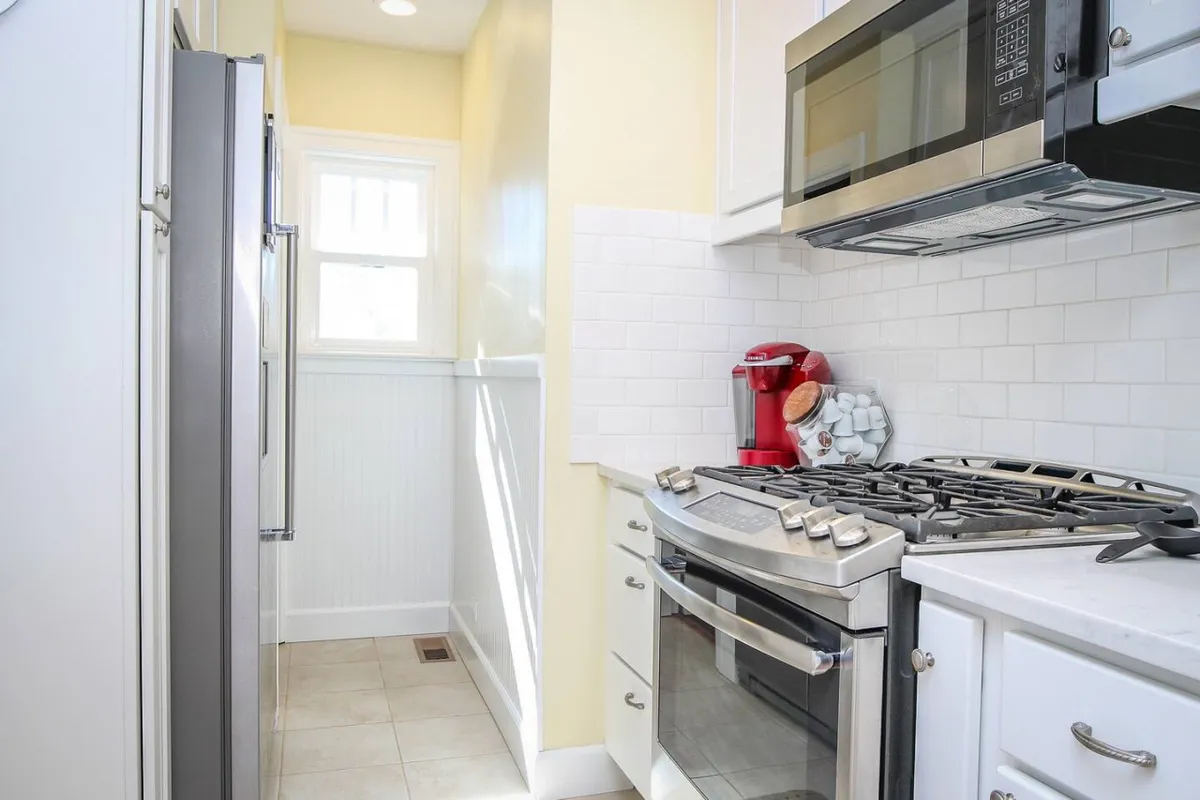 A stylish, newly remodeled kitchen featuring stainless steel appliances, a gas stove, a vibrant red coffee maker, and a classic white subway tile backsplash. The space is clearly set up for both quick breakfasts and elaborate meal prep.