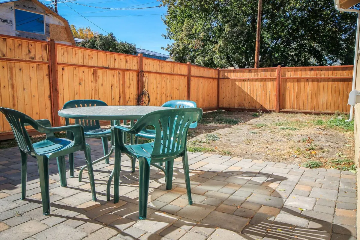 This image shows a backyard with a table and chairs set up for outdoor dining, all bordered by a sturdy wooden fence. The setting is casual, bright, and perfect for family meals or evening relaxation. The open space suggests room for pets or children to play safely.
